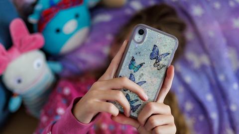 Ein Mädchen liegt in ihrem Bett und ist am Handy.