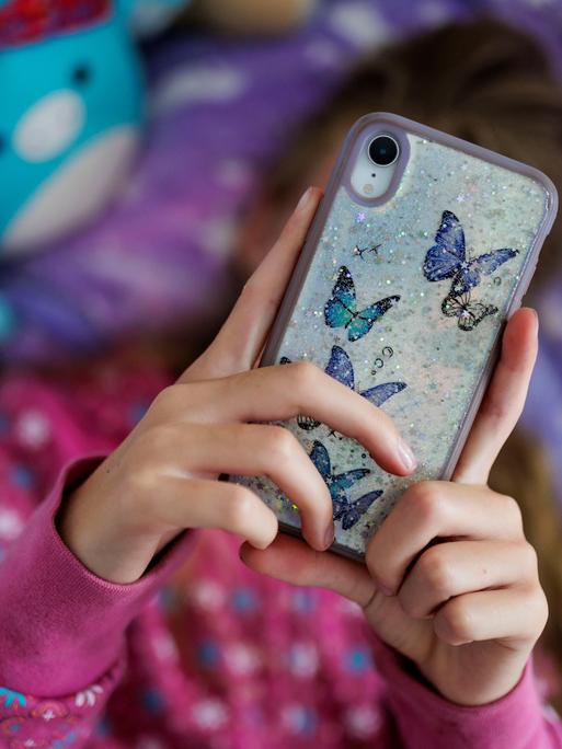 Ein Mädchen liegt in ihrem Bett und ist am Handy.