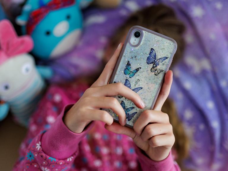 Ein Mädchen liegt in ihrem Bett und ist am Handy.