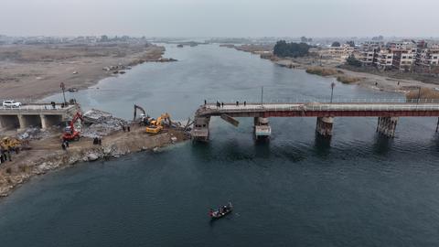 Luftaufnahme einer über einen Fluss führenden Brücke, die an einer Stelle eingestürzt ist. Drum herum stehen Kräne und Traktoren.
