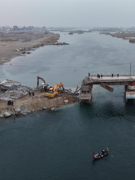 Luftaufnahme einer über einen Fluss führenden Brücke, die an einer Stelle eingestürzt ist. Drum herum stehen Kräne und Traktoren.