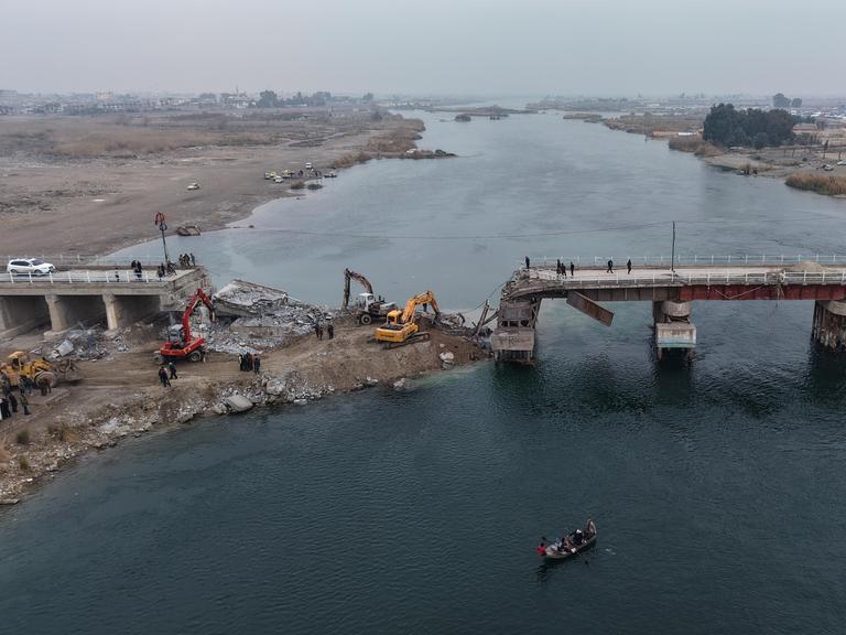 Luftaufnahme einer über einen Fluss führenden Brücke, die an einer Stelle eingestürzt ist. Drum herum stehen Kräne und Traktoren.