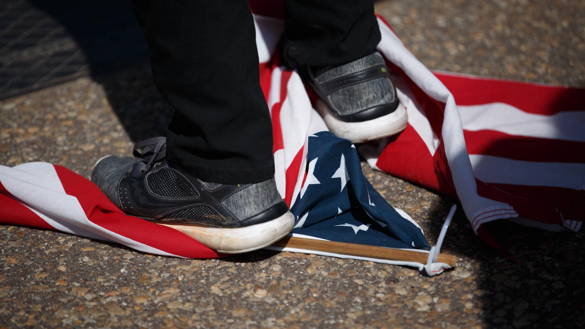 Großaufnahme eines Fußes, der auf einer am Boden liegenden us-amerikanischen Flagge steht.