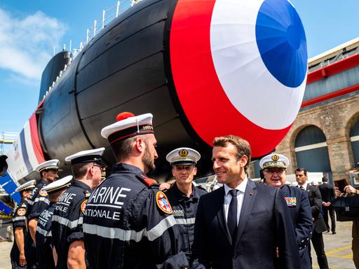 Der französische Präsident Macron spricht mit einem Mitarbeiter der Marine. Im Hintergrund steht ein U-Boot.