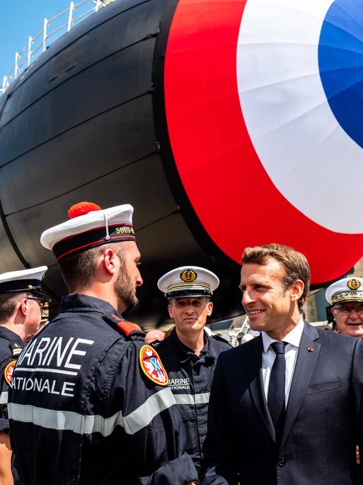 Der französische Präsident Macron spricht mit einem Mitarbeiter der Marine. Im Hintergrund steht ein U-Boot.