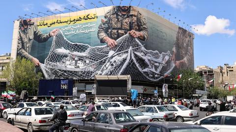 Ein iranisches Propagandaplakat zeigt Soldaten, die ein Fischernetz voller Schiffe zusammenziehen.