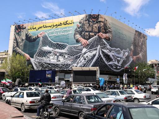 Ein iranisches Propagandaplakat zeigt Soldaten, die ein Fischernetz voller Schiffe zusammenziehen.