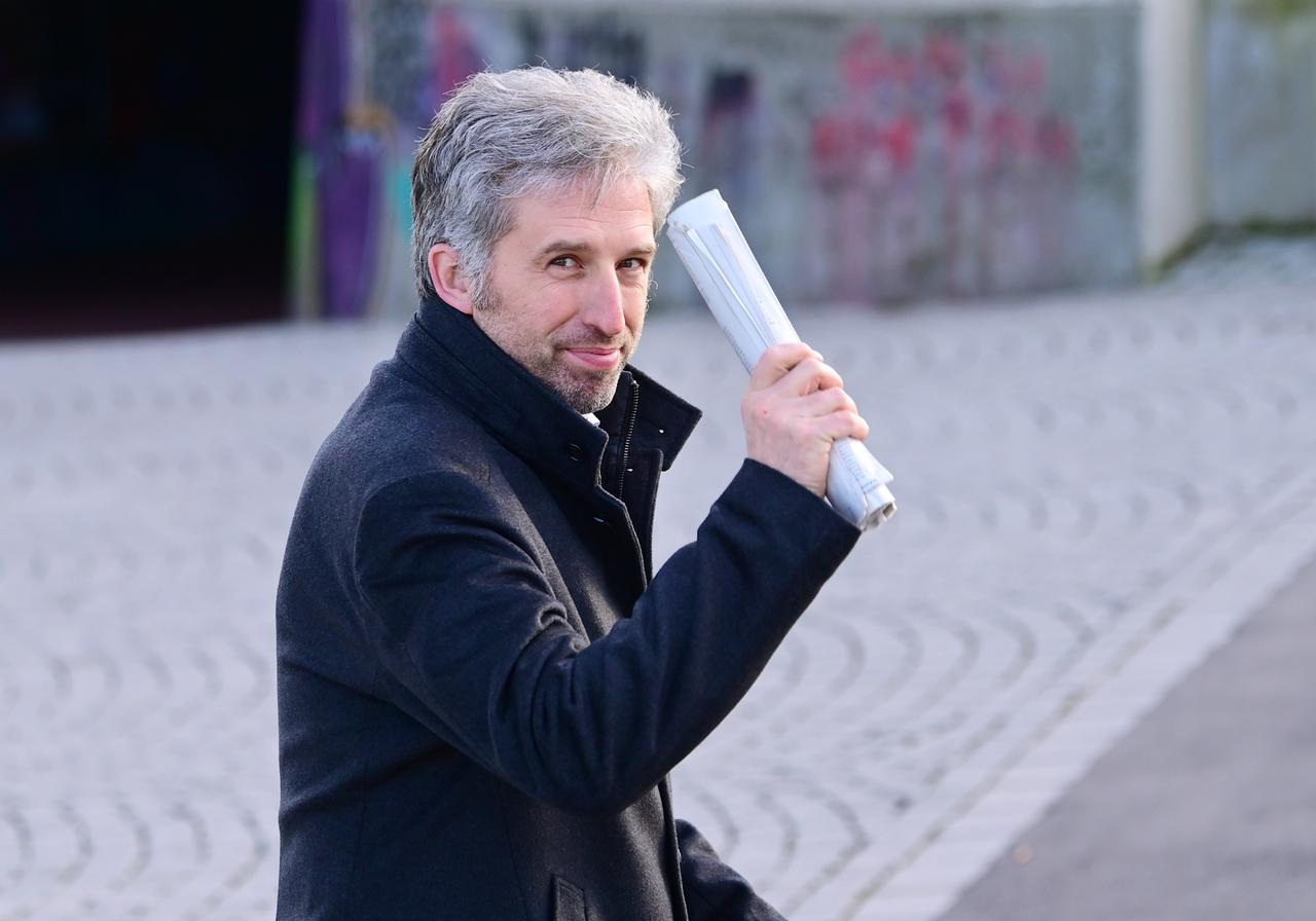 Tübingens Oberbürgermeister Boris Palmer winkt mit einem zusammengerollten Papierstapel in die Kamera.