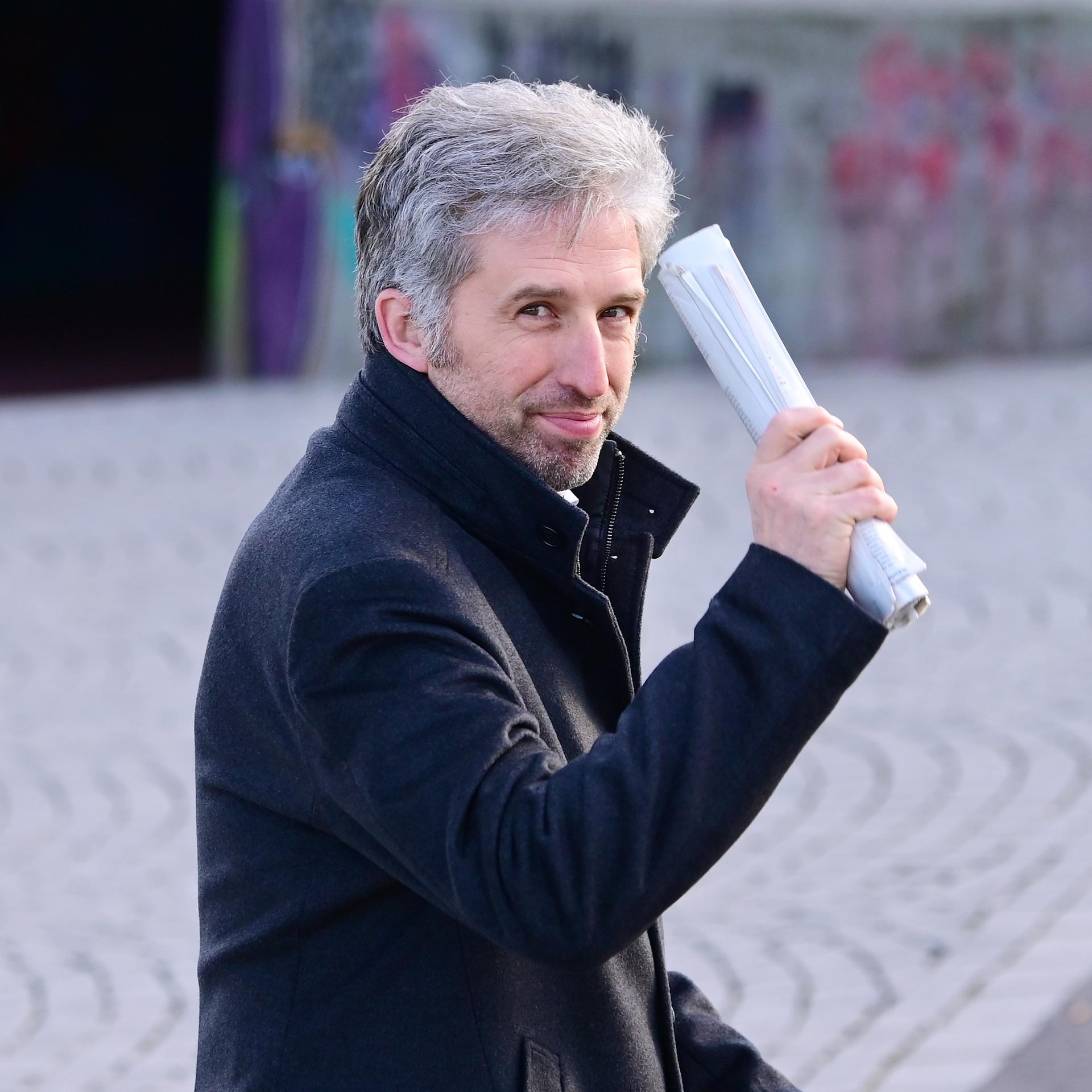 Tübingens Oberbürgermeister Boris Palmer winkt mit einem zusammengerollten Papierstapel in die Kamera.