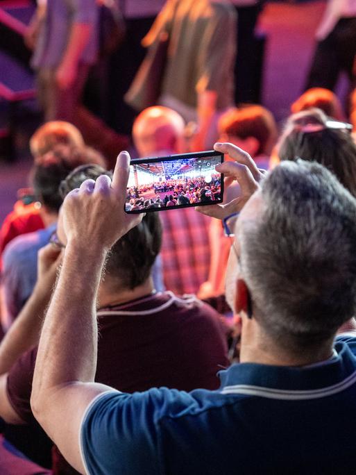 Ein Mann steht im Publikum der re:publica und macht mit seinem Smartphone ein Foto von der Bühne.