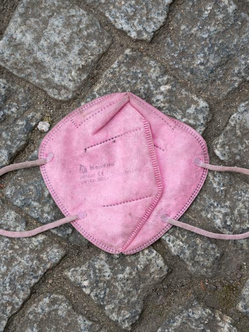 Eine weggeworfene rosafarbene FFP2-Schutzmaske gegen Corona (Covid-19) liegt auf einem gepflasterten Boden.
