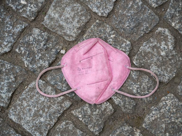 Eine weggeworfene rosafarbene FFP2-Schutzmaske gegen Corona (Covid-19) liegt auf einem gepflasterten Boden.
