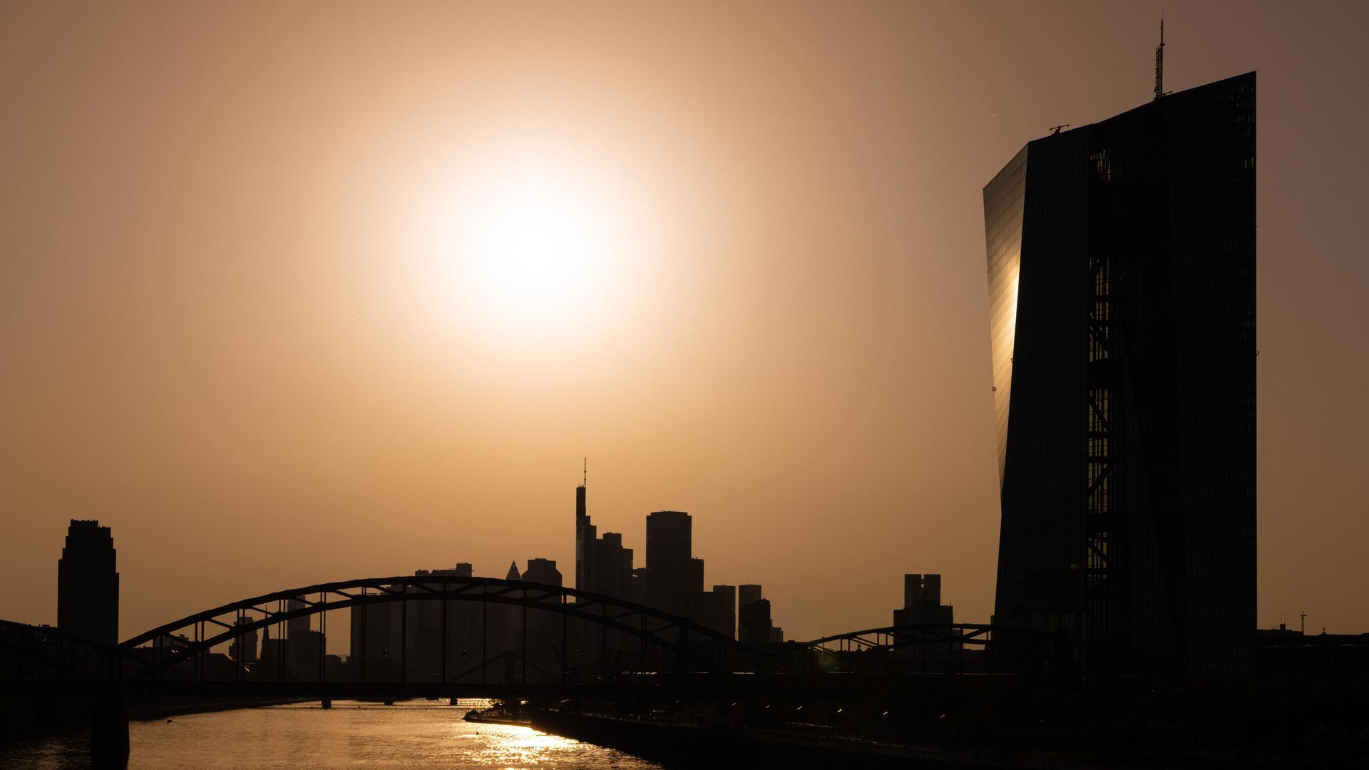 Die Sonne steht hoch über der Europäischen Zentralbank (EZB) und der Frankfurter Bankenskyline.