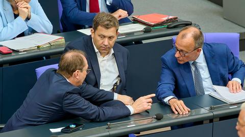 Bundeskanzler Merz (CDU), Vizekanzler Klingbeil (SPD) und Innenminister Dobrindt (CSU) unterhalten sich im Plenarsaal sitzend im Bundestag.