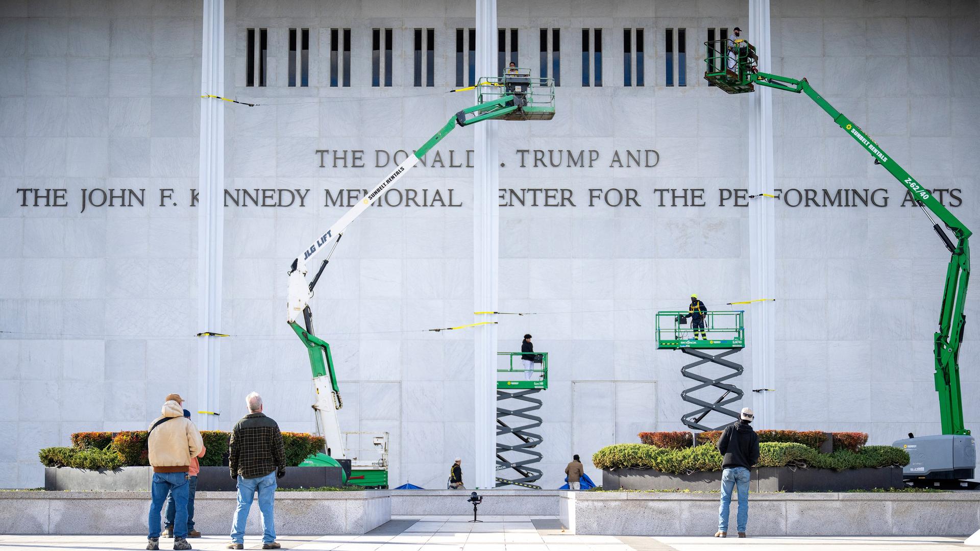 Arbeiter haben den neuen Schriftzug am Kennedy-Center in Washington DC angebracht. Auf dem Bild sind noch vier Hebebühnen zu sehen.