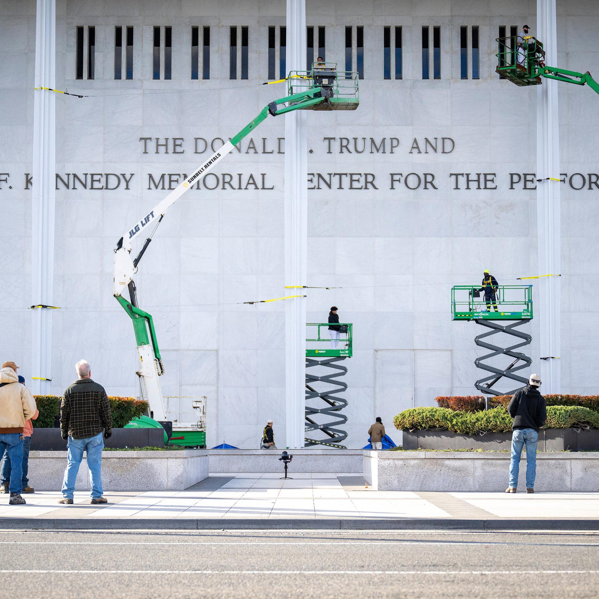 Arbeiter haben den neuen Schriftzug am Kennedy-Center in Washington DC angebracht. Auf dem Bild sind noch vier Hebebühnen zu sehen.