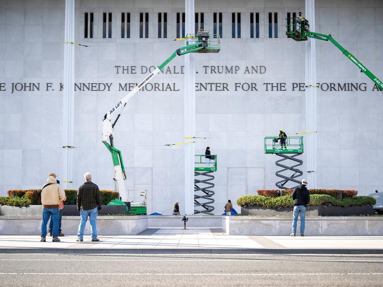Arbeiter haben den neuen Schriftzug am Kennedy Center in Washington DC angebracht. Auf dem Bild sind noch vier Hebebühnen zu sehen.