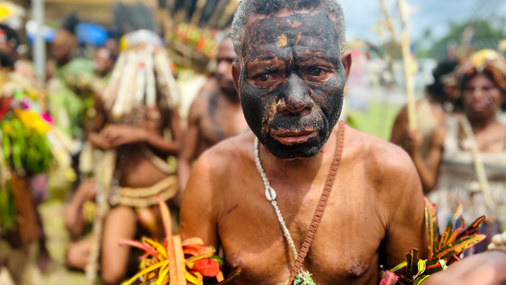 Ein Mann in traditioneller Tracht und mit schwarz bemaltem Gesicht aus dem Inselstaat Papua-Neuguinea schaut traurig.