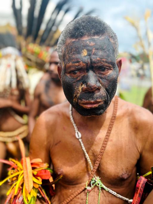 Ein Mann in traditioneller Tracht und mit schwarz bemaltem Gesicht aus dem Inselstaat Papua-Neuguinea schaut traurig.