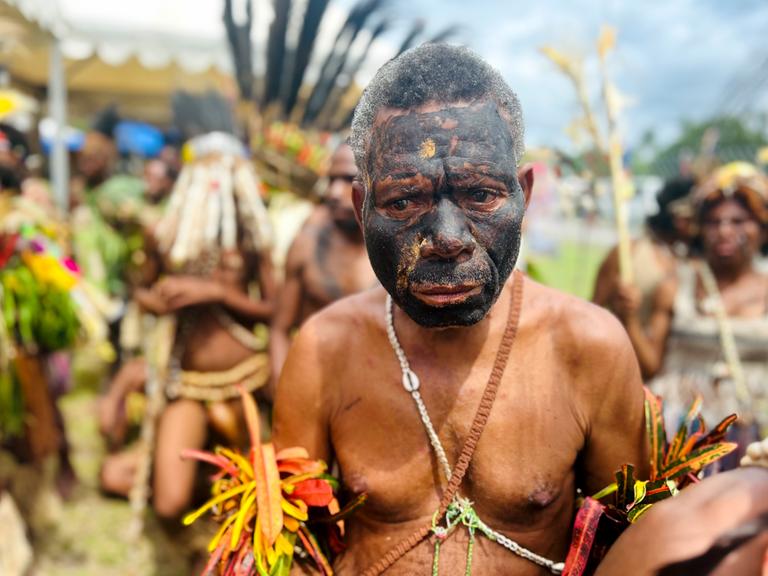 Ein Mann in traditioneller Tracht und mit schwarz bemaltem Gesicht aus dem Inselstaat Papua-Neuguinea schaut traurig.