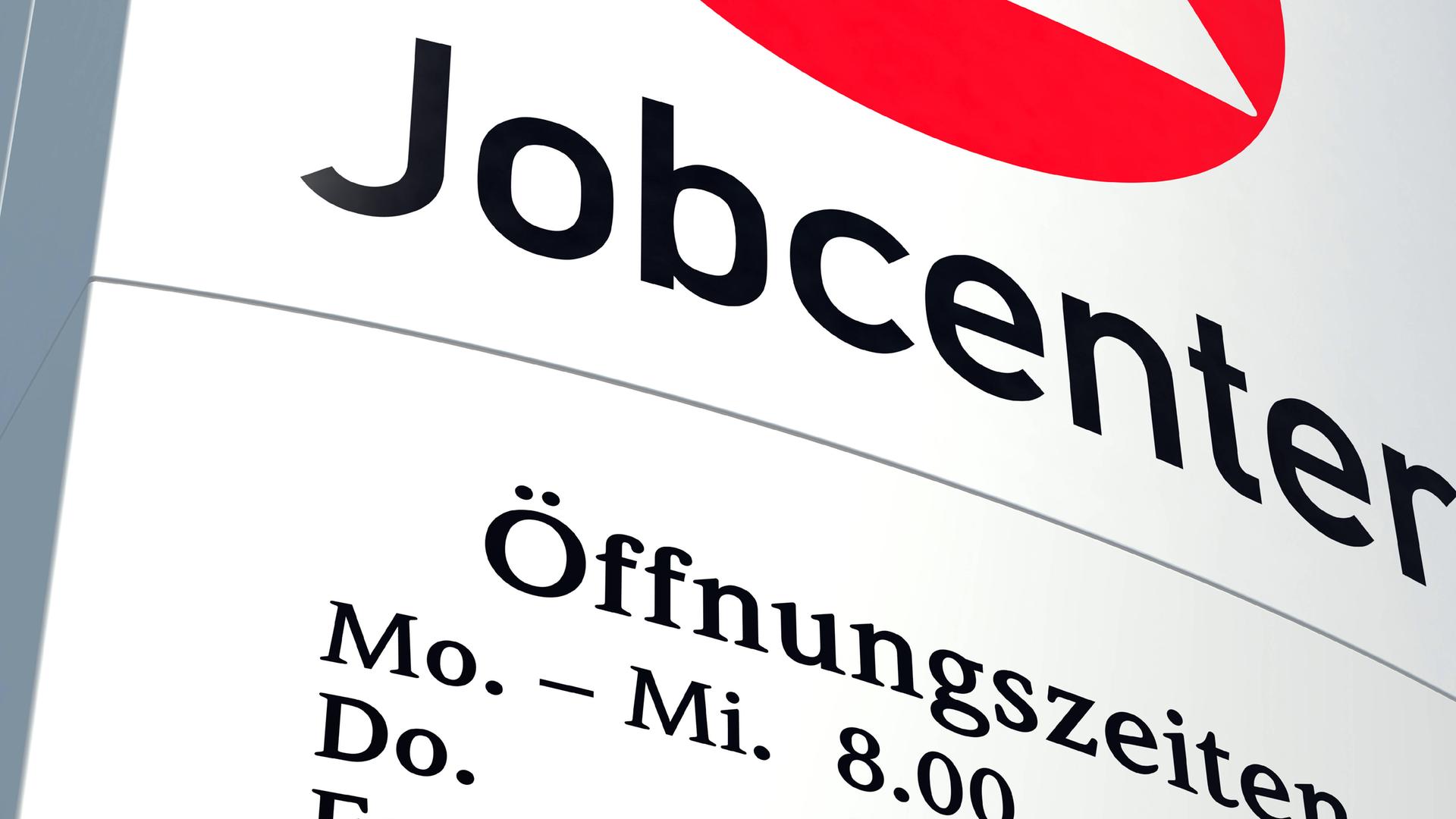 Ein Schild des Jobcenters, auf dem zum Teil die Öffnungszeiten zu lesen sind. 