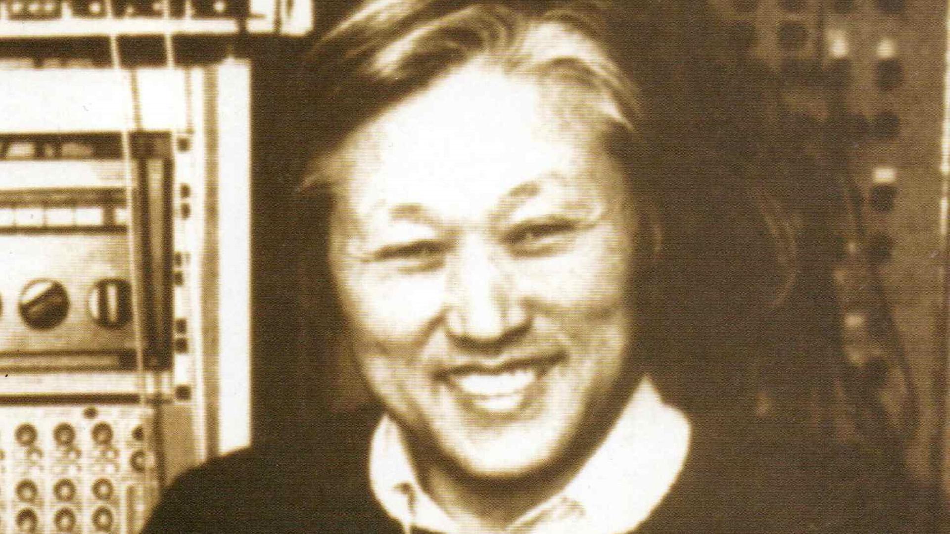 Ein monochromes Portrait von Sukhi Kang, der mit einem Bandkarton unter dem Arm in die Kamera lächelt. Ein monochromes Portrait von Sukhi Kang, der mit einem Bandkarton unter dem Arm in die Kamera lächelt.