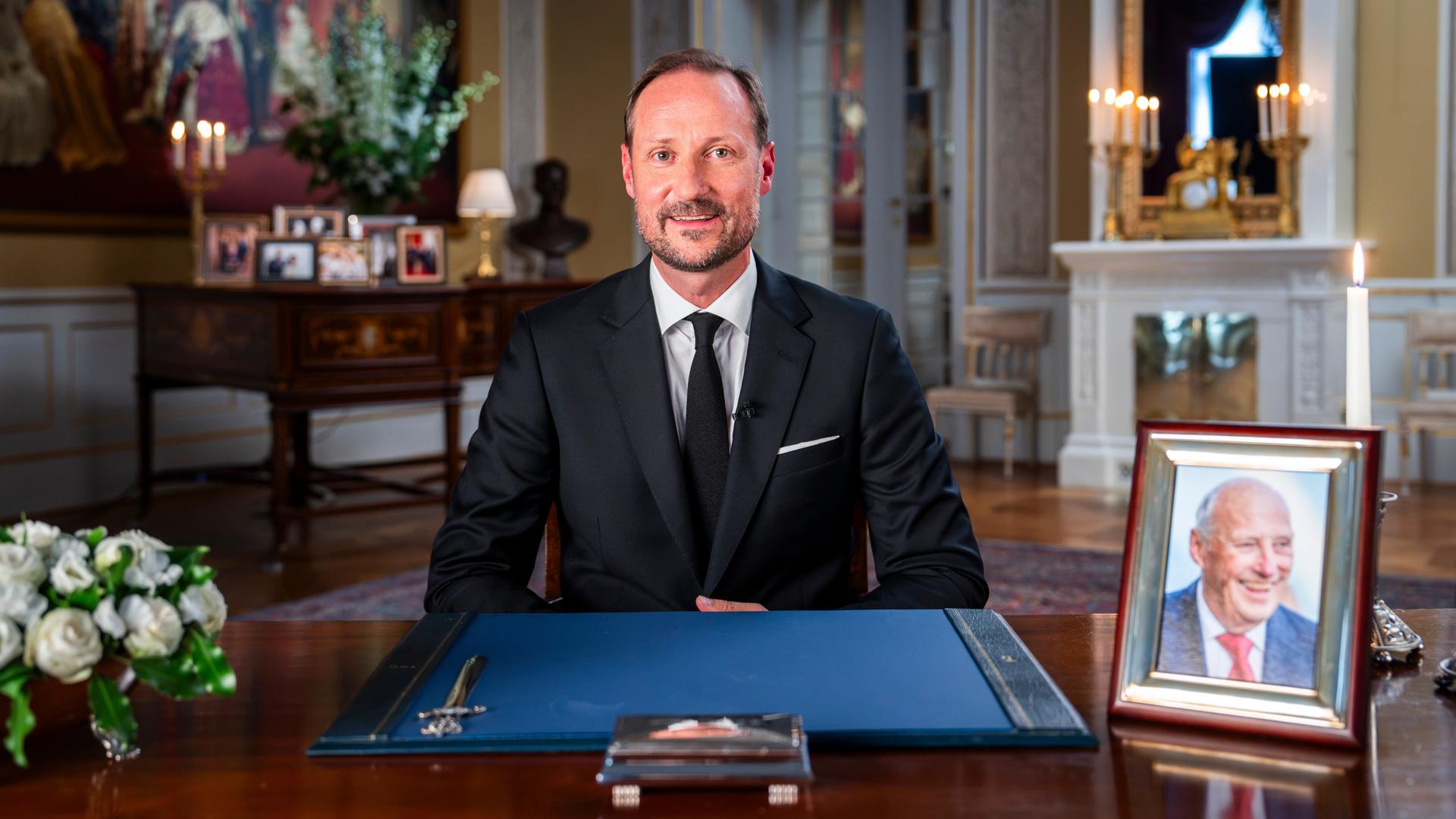 Der neue norwegische König Haakon VIII. sitzt bei einer Ansprache aus dem Palast an einem Schreibtisch. Darauf stehen Blumen und ein Foto seines verstorbenen Vaters Harald. Der neue norwegische König Haakon VIII. sitzt bei einer Ansprache aus dem Palast an einem Schreibtisch. Darauf stehen Blumen und ein Foto seines verstorbenen Vaters Harald.