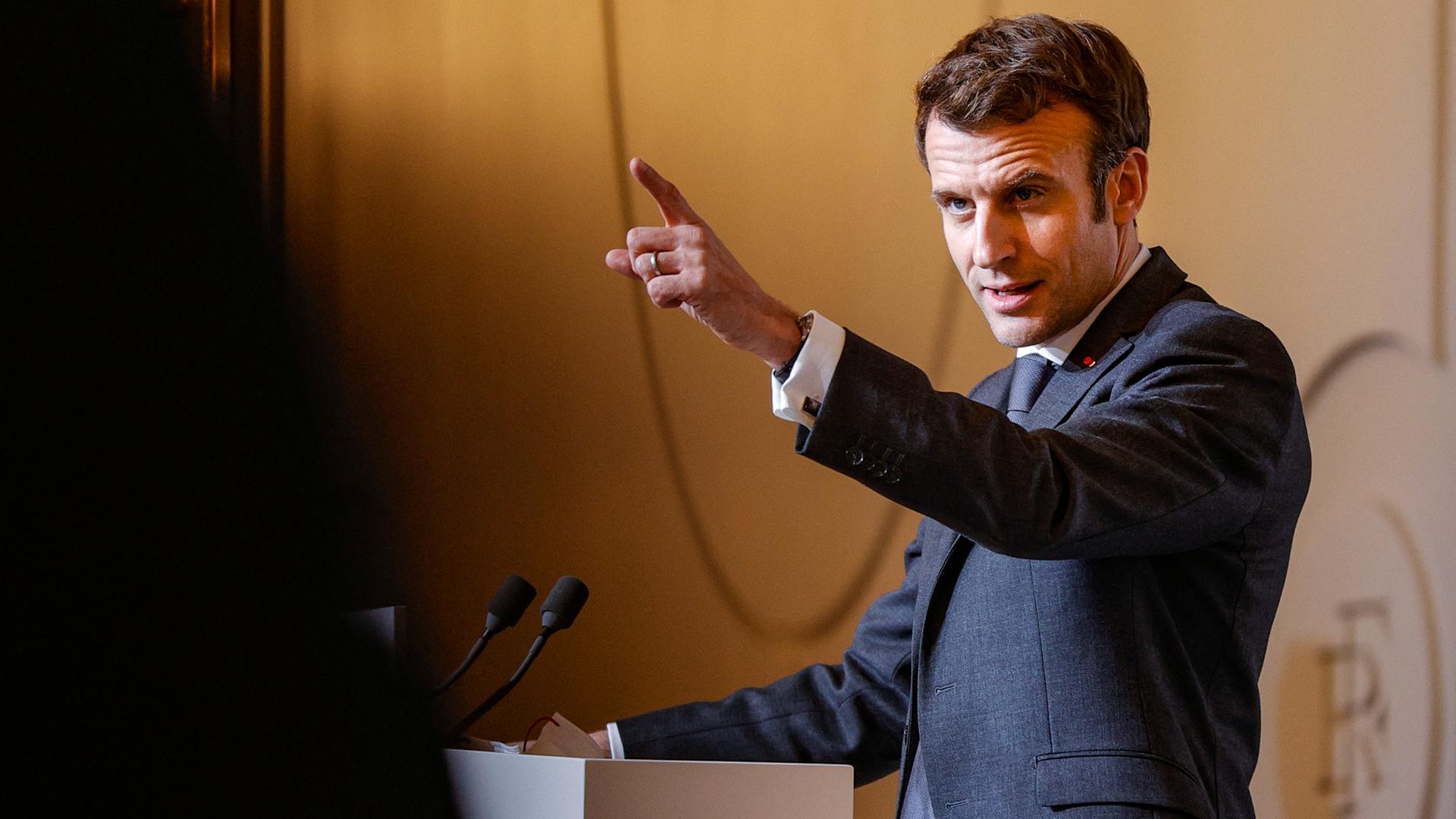 Emmanuel Macron spricht an einem Rednerpult und streckt den Zeigefinger in einer zukunftsweisenden Geste in die Luft.