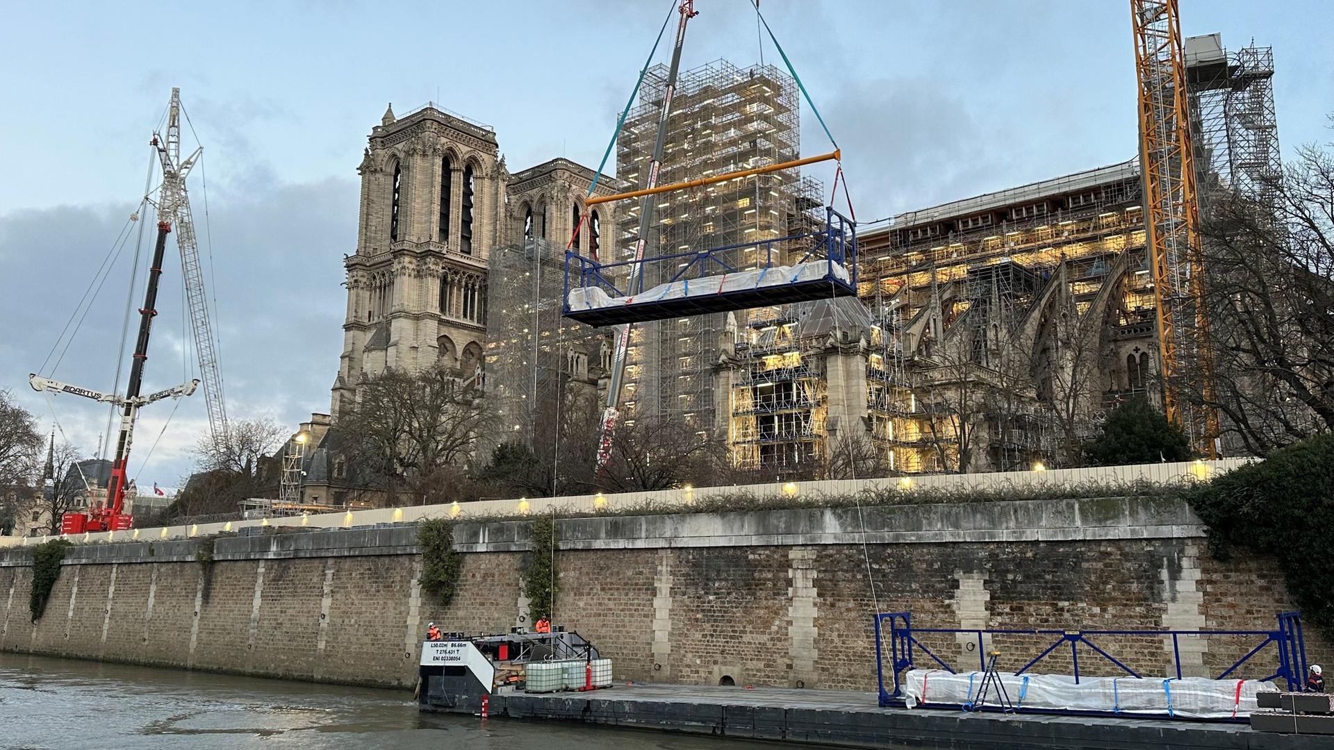 Die Baustelle der Kathedrale Notre-Dame in Paris vom Ufer der Seine aus gesehen, ein Baukran hebt Material in die Luft. Die Baustelle der Kathedrale Notre-Dame in Paris vom Ufer der Seine aus gesehen, ein Baukran hebt Material in die Luft.