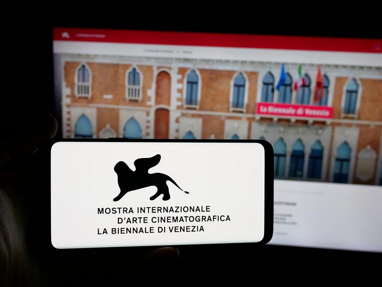 Auf dieser Fotoillustration hält eine Person ein Smartphone in der Hand, auf dessen Bildschirm das Logo der Filmfestspiele von Venedig (Biennale) vor einer Website zu sehen ist.
Auf dieser Fotoillustration hält eine Person ein Smartphone in der Hand, auf dessen Bildschirm das Logo der Filmfestspiele von Venedig (Biennale) vor einer Website zu sehen ist.