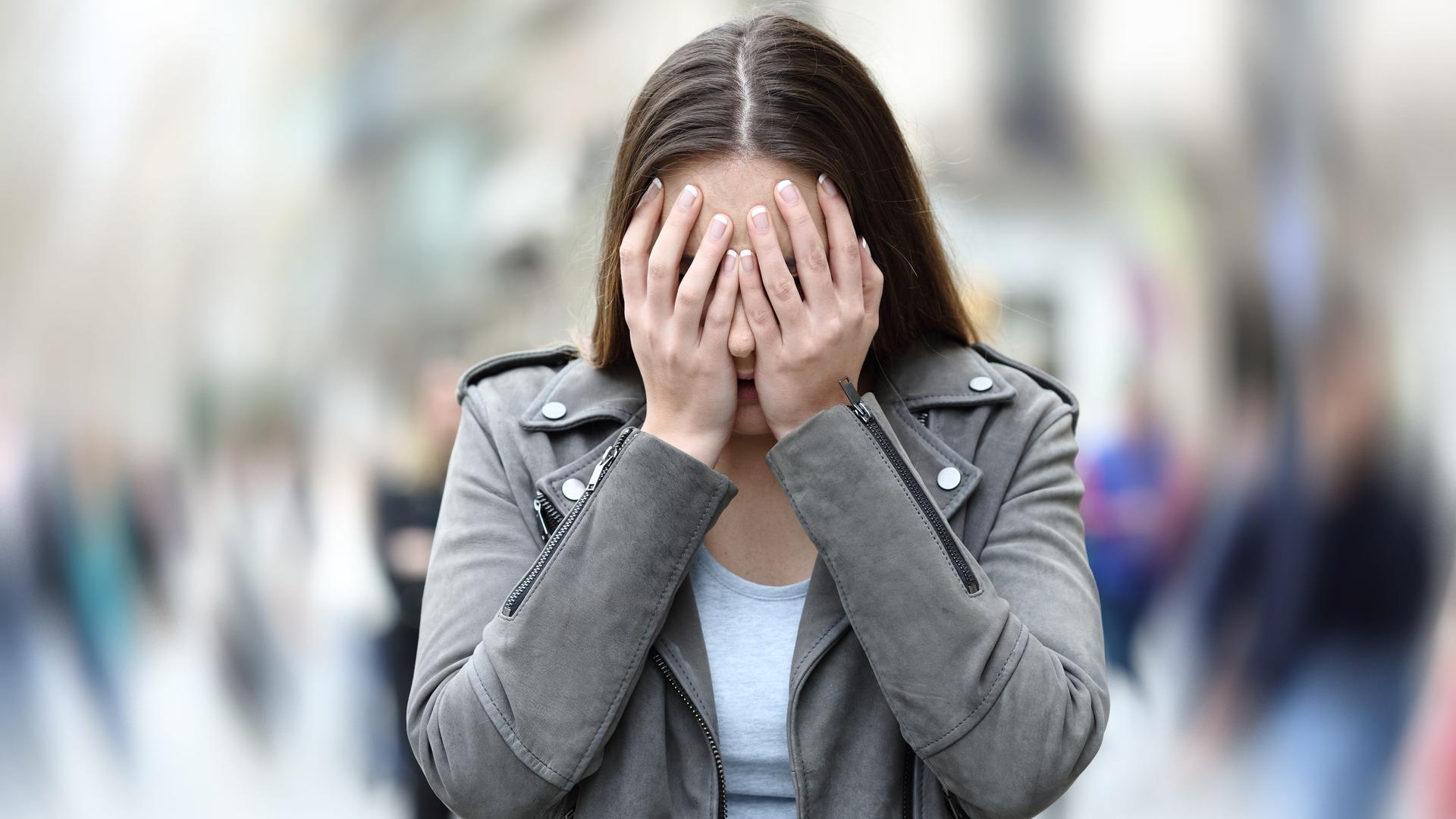 Eine Frau versteckt ihr Gesicht hinter ihren Händen. Der Hintergrund hinter ihr ist verschwommen.