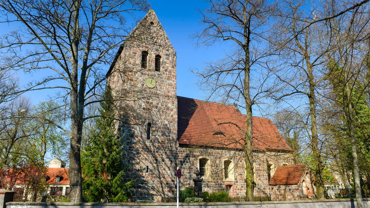 Eine alte Kirche im Sonnenschein. Sie steht inmitten von Bäumen.