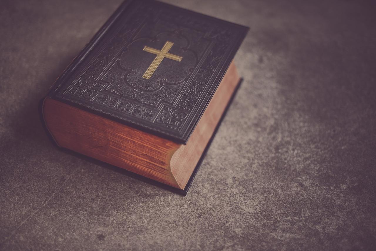 Eine schwere, dunkle Bibel mit einem goldenen Kreuz auf dem Deckel liegt auf einem Tisch.