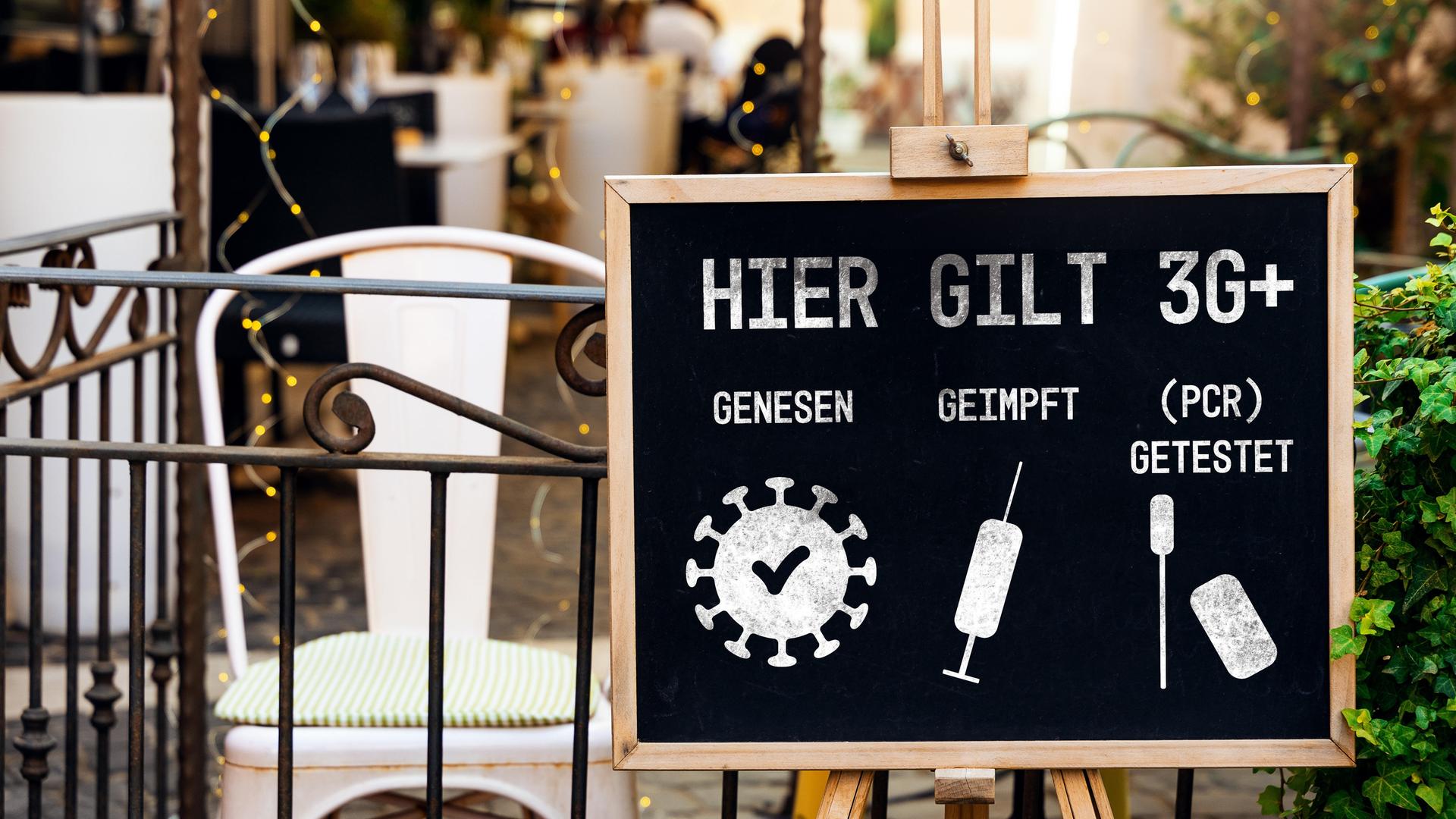 Tafel mit der Aufschrift "Hier gilt 3G+: genesen, geimpft, (PCR) getestet" vor einem Café als Schutzmaßnahme gegen die weitere Verbreitung des Coronavirus