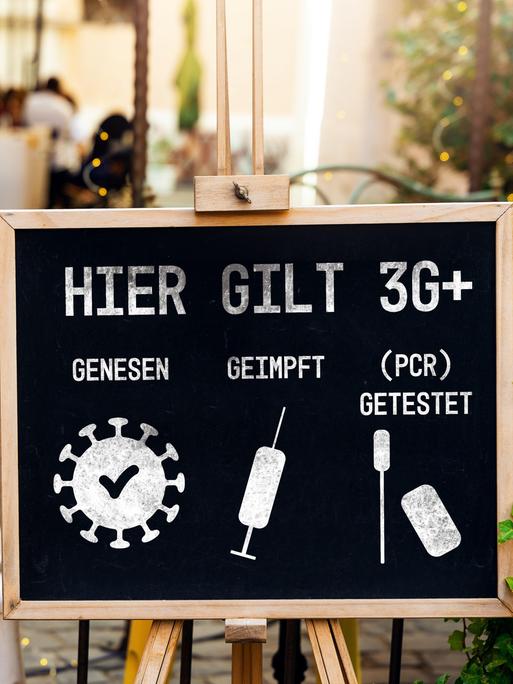 Tafel mit der Aufschrift "Hier gilt 3G+: genesen, geimpft, (PCR) getestet" vor einem Café als Schutzmaßnahme gegen die weitere Verbreitung des Coronavirus