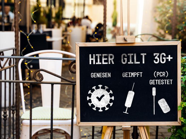 Tafel mit der Aufschrift "Hier gilt 3G+: genesen, geimpft, (PCR) getestet" vor einem Café als Schutzmaßnahme gegen die weitere Verbreitung des Coronavirus