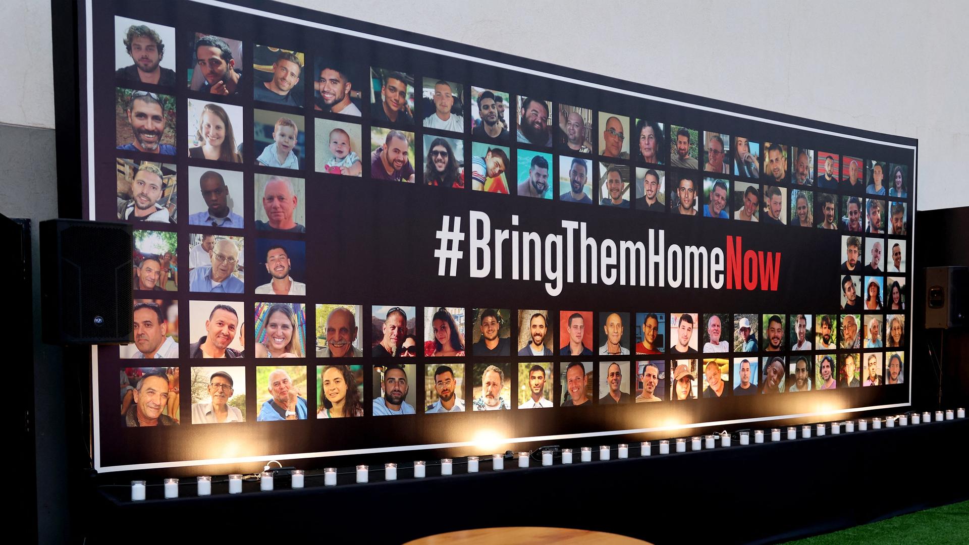 Portraits der von der Hamas verschleppten Geiseln an einer Wand. Dort ist die Aufforderung "Bring Them Home Now" zu lesen. 