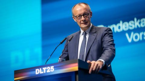 Merz steht an einem Rednerpult auf der Bühne. Auf dem Pult ist das Logo des Deutschlandtags abgebildet: DLT25.