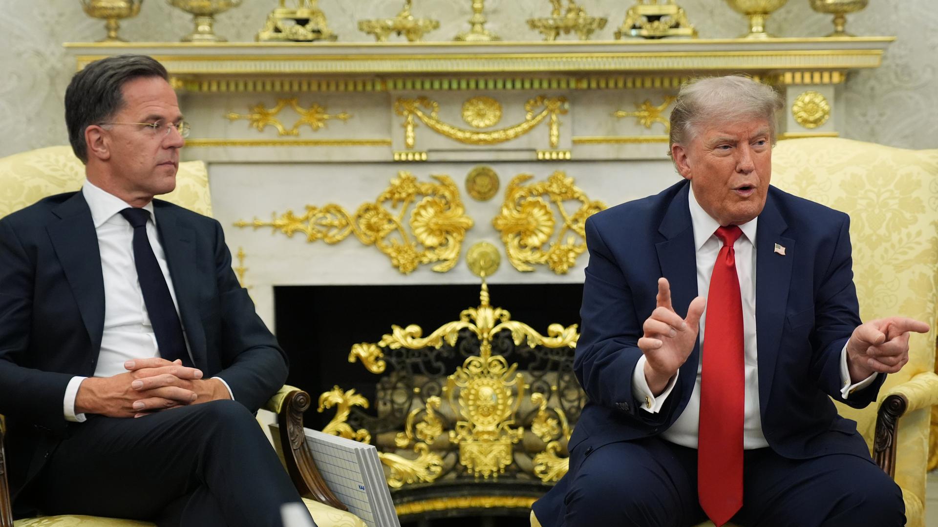 NATO-Generalsekretär Rute und US-Präsident Trump sitzen im Oval Office des Weißen Hauses in Sesseln nebeneinander. Trump hölt gestikulierend eine Ansprache, Rutte schaut ihm dabei zu.