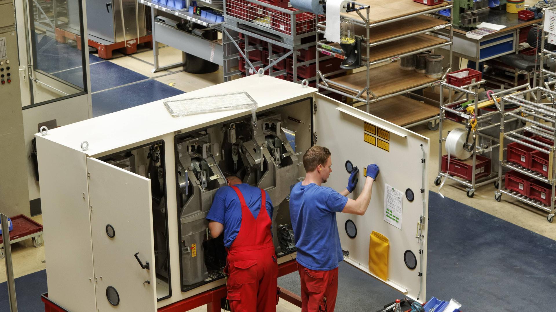 Montage von Hochspannungsschaltern und Schaltanlagen im Siemens Schaltwerk in Berlin-Siemensstadt. Zwei Arbeiter stehen vor einer Schaltanlage.