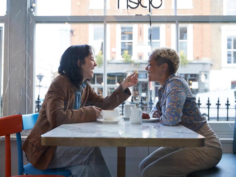 Zwei Frauen sitzen sich lächelnd in einem Café gegenüber