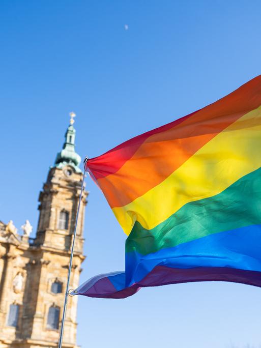 Eine Regenbogenfahne weht vor einer Kirche.