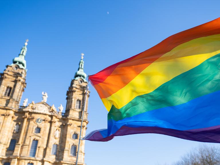 Eine Regenbogenfahne weht vor einer Kirche.