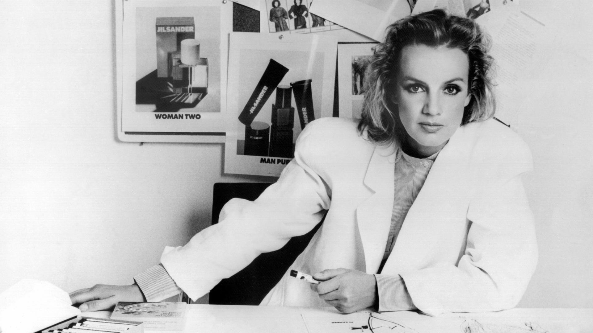 Die deutsche Modedesignerin Jil Sander sitzt 1983 in ihrem Büro hinter einem Schreibtisch.
