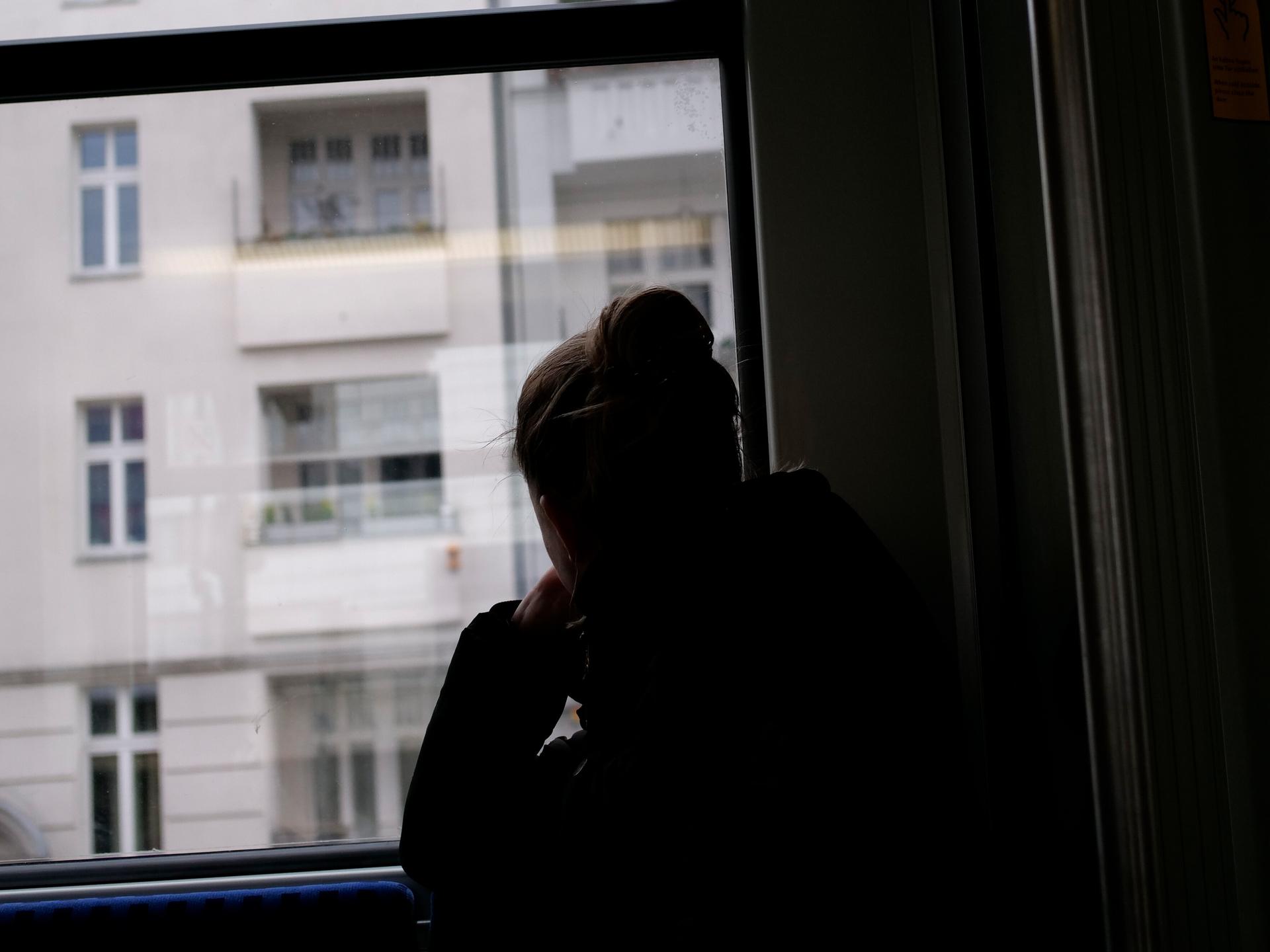 Eine junge Frau sitzt in einer Bahn und blickt, abgewendet von den anderen Fahrgästen, aus dem Fenster. 