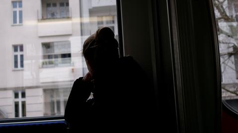 Eine junge Frau sitzt in einer Bahn und blickt, abgewendet von den anderen Fahrgästen, aus dem Fenster. 