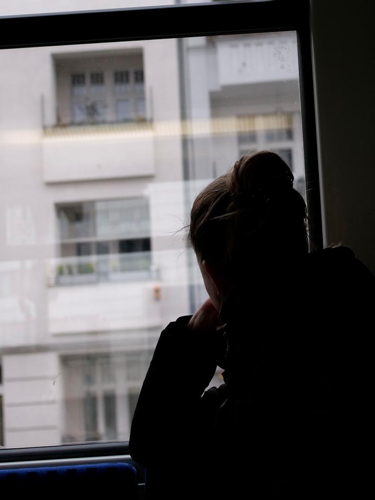 Eine junge Frau sitzt in einer Bahn und blickt, abgewendet von den anderen Fahrgästen, aus dem Fenster. 
