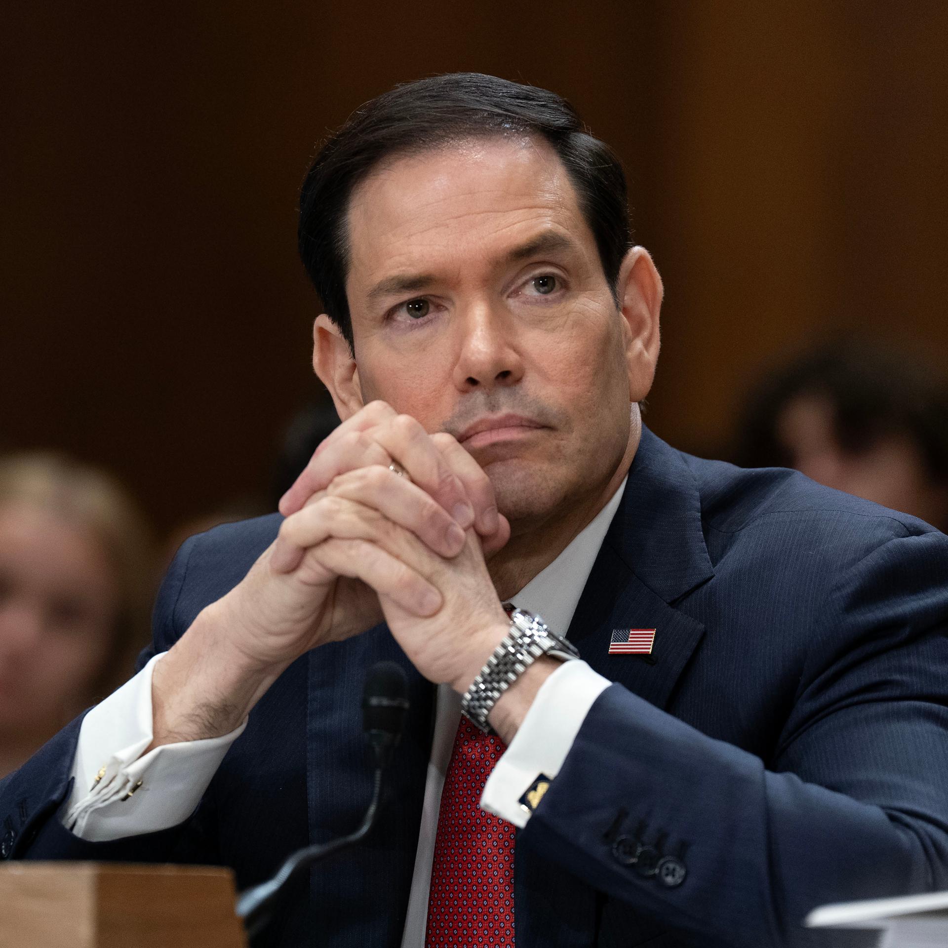 US-Außenminister Marco Rubio schaut nachdenklich und hat seine Hände auf dem Tisch aufgestützt und gefaltet. 