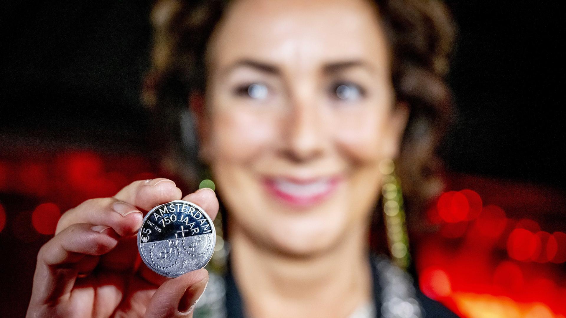 Eine Frau hält eine Münze nach vorne, auf der "750 Jahre Amsterdam" steht.