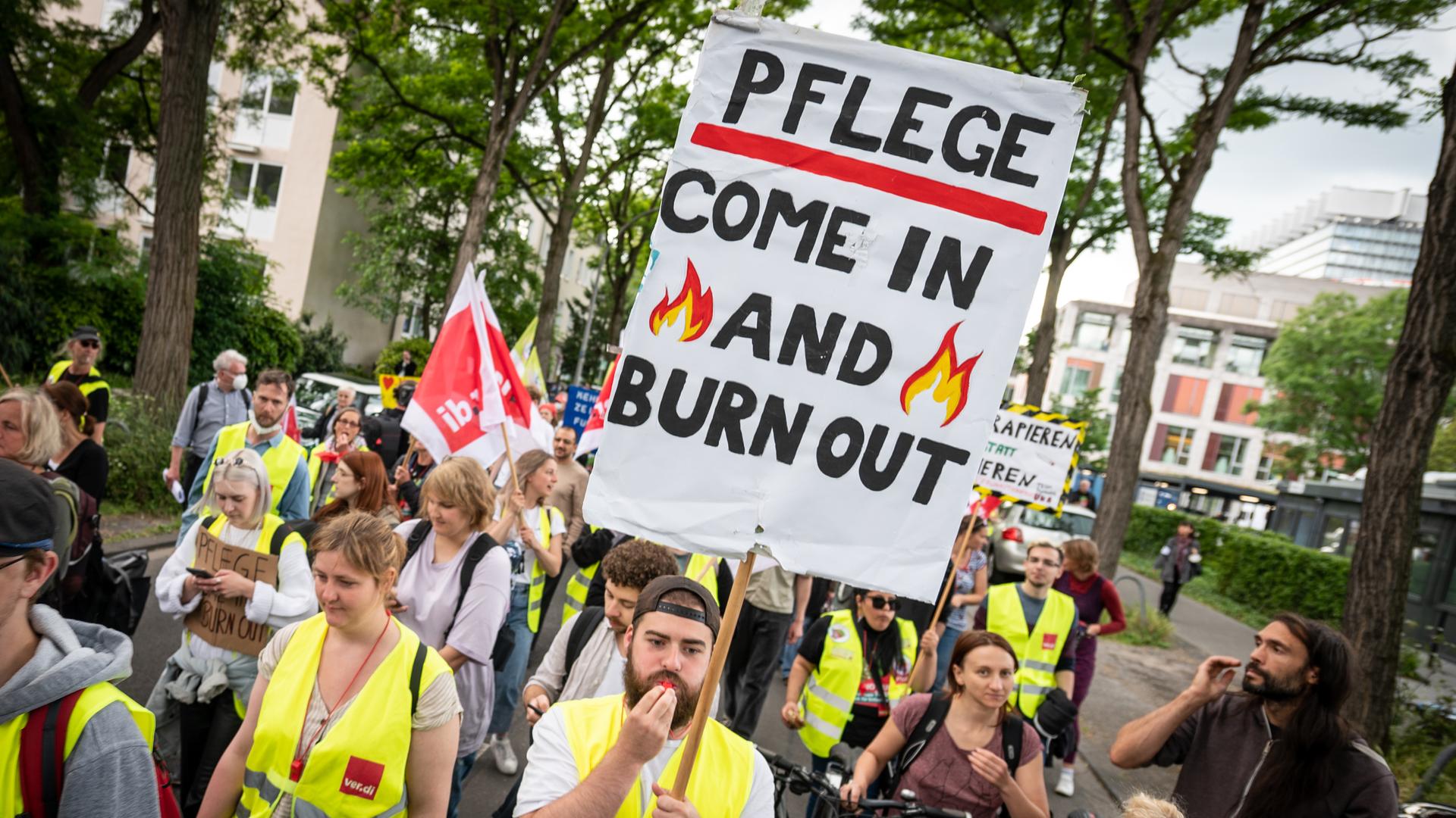 Mit einem Plakat "Pflege - come in and burn out" nehmen Pflegekräfte an einer Demonstration teil. 